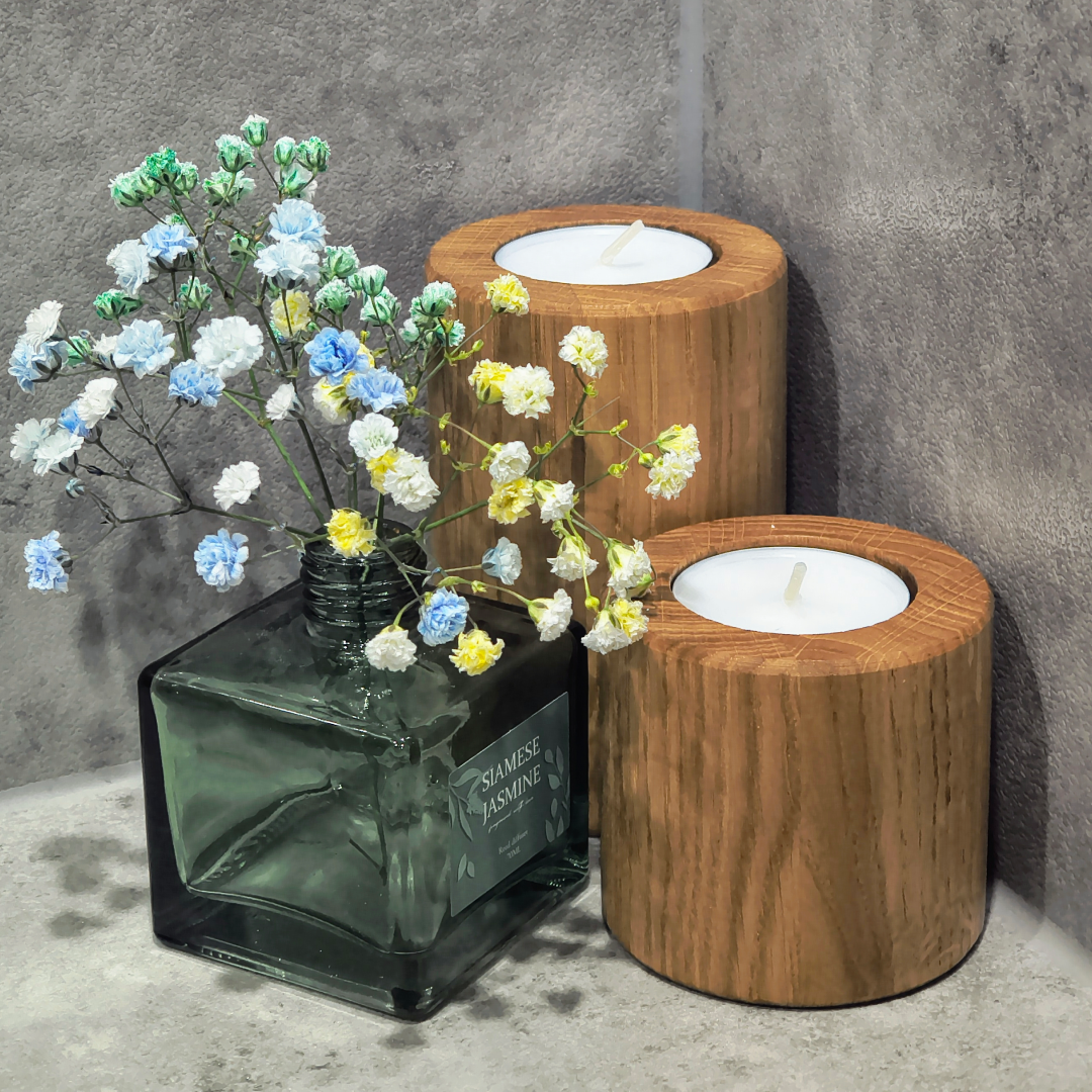Dwa drewniane świeczniki na tealighty obok zielonego flakonu z niebiesko-żółtymi kwiatami gipsówki