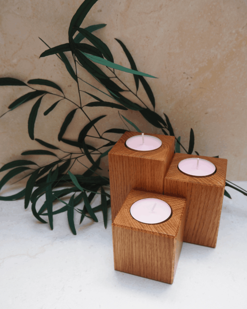 Trzy drewniane dębowe świeczniki na tealighty o różnych wysokościach, w pobliżu ozdobnej zielonej gałązki