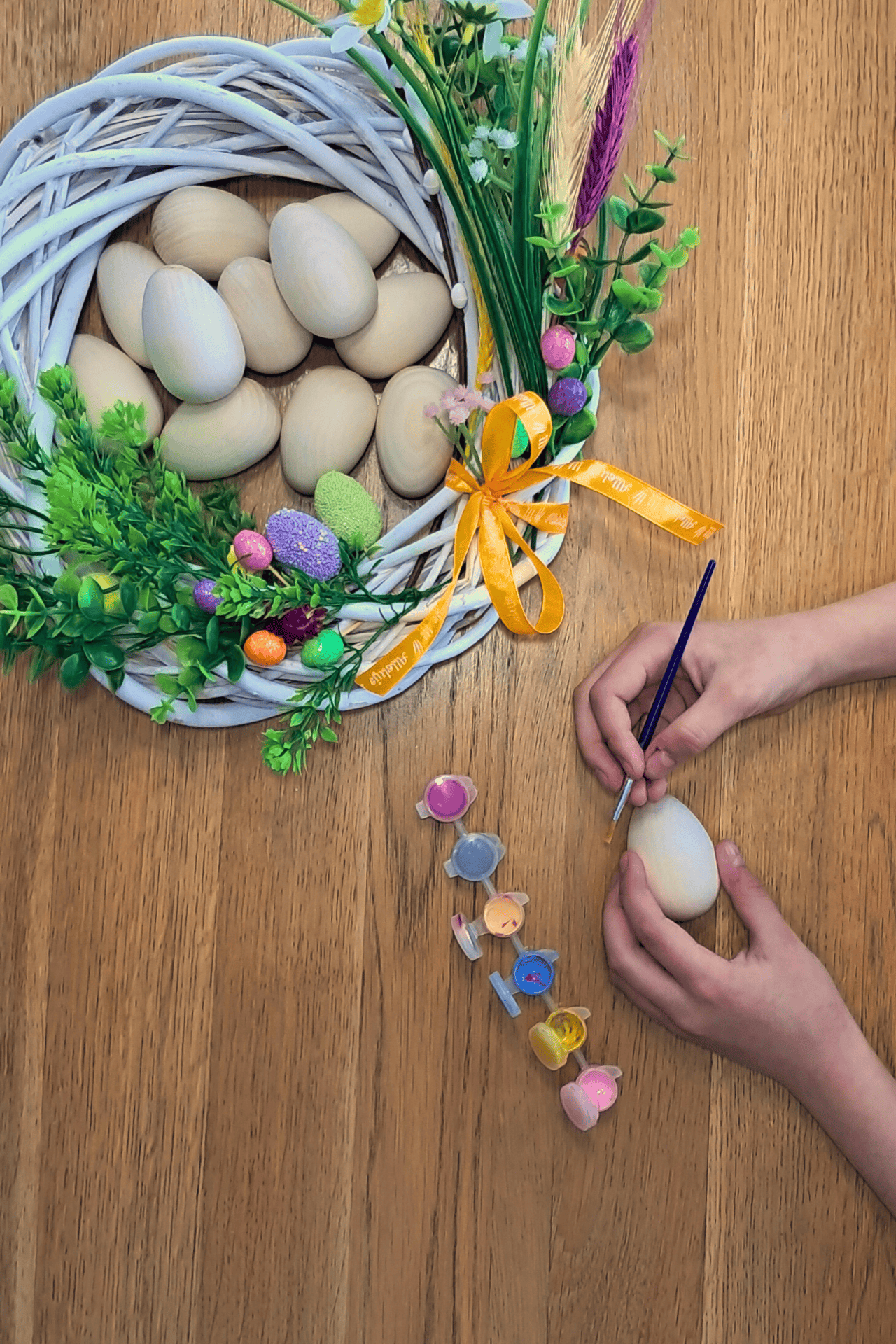 Drewniane jajka w ozdobie wielkanocnej i ręce osoby zdobiącej drewniane jajko farbami