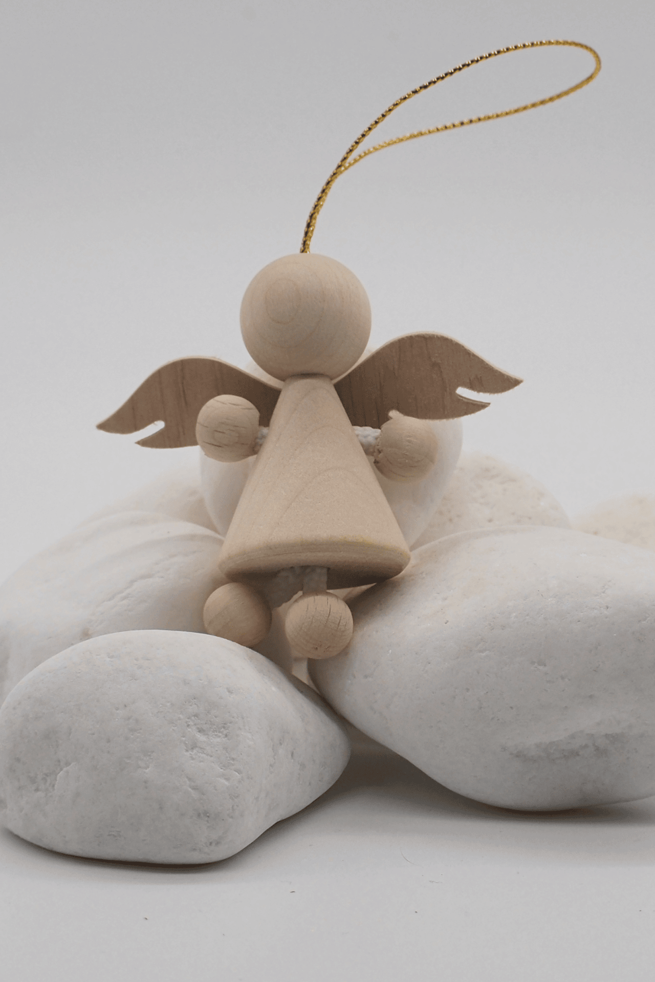 Drewniany aniołek zawieszka z jasnego drewna ze złotą zawieszką, siedzący na białych ozdobnych kamieniach