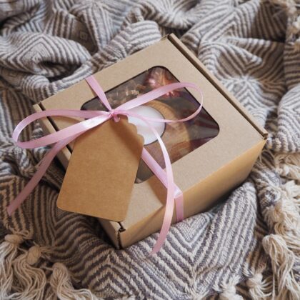 Gotowy box prezentowy, zapakowany w eko pudełko z okienkiem, ozdobiony różową wstążką wraz z eko bilecikiem. W środku znajduje się drewniany świecznik ze świecą tealight oraz suszony kwiat