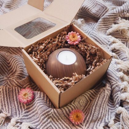 Zestaw prezentowy opakowany w eko pudełko z okienkiem. W środku znajduje się drewniany świecznik na tealighty z białą świecą oraz suszonym, ozdobnym kwiatem.