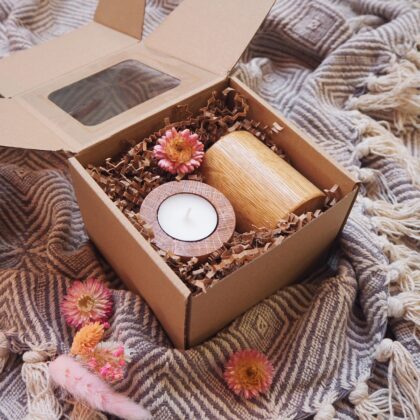 Zestaw drewnianych świeczników na prezent o kształcie walca. Zapakowane w eko pudełko z okienkiem. W środku pudełka znajduje się jasno brązowy papierowy wypełniacz oraz ozdobny suszony kwiat.