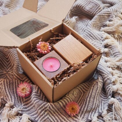 Box prezentowy, eko pudełko z okienkiem, w środku dwa świeczniki na tealighty o kształcie kostki, z drewna dębowego. Świeczniki posiadają różową świeczkę. Obok znajduje się ozdobny suszony różowy kwiat.