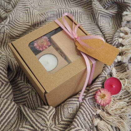 Gotowy prezent - eko pudełko z okienkiem, w środku dwa drewniane, jasne świeczniki na tealighty z białą świecą oraz różowy suszony kwiat. Pudełko oplecione różową wstążką z eko bilecikiem.