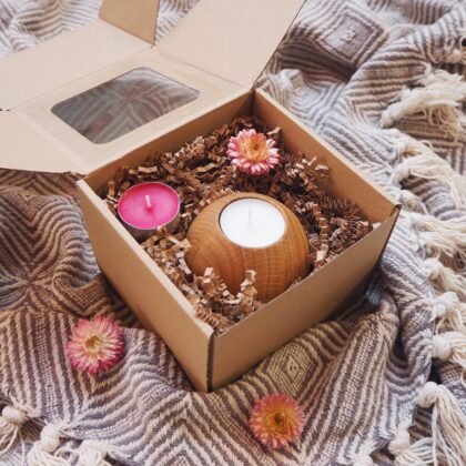 Box prezentowy, w eko pudełku znajduje się drewniany świecznik na tealighty z białą świecą. Obok różowa świeca podgrzewacz i suszony różowy kwiat.